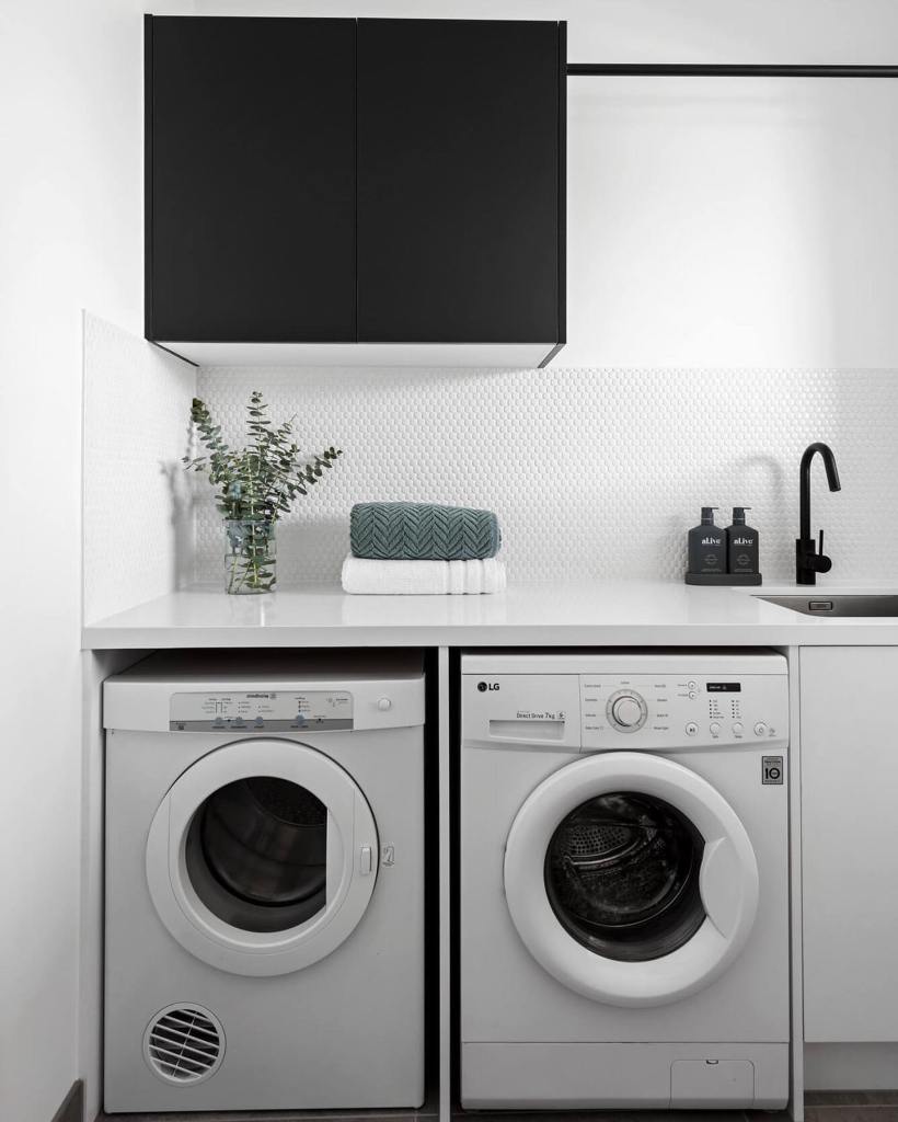 A modern laundry room with a white countertop and a white LG washing machine, accompanied by a black faucet and a black ca...