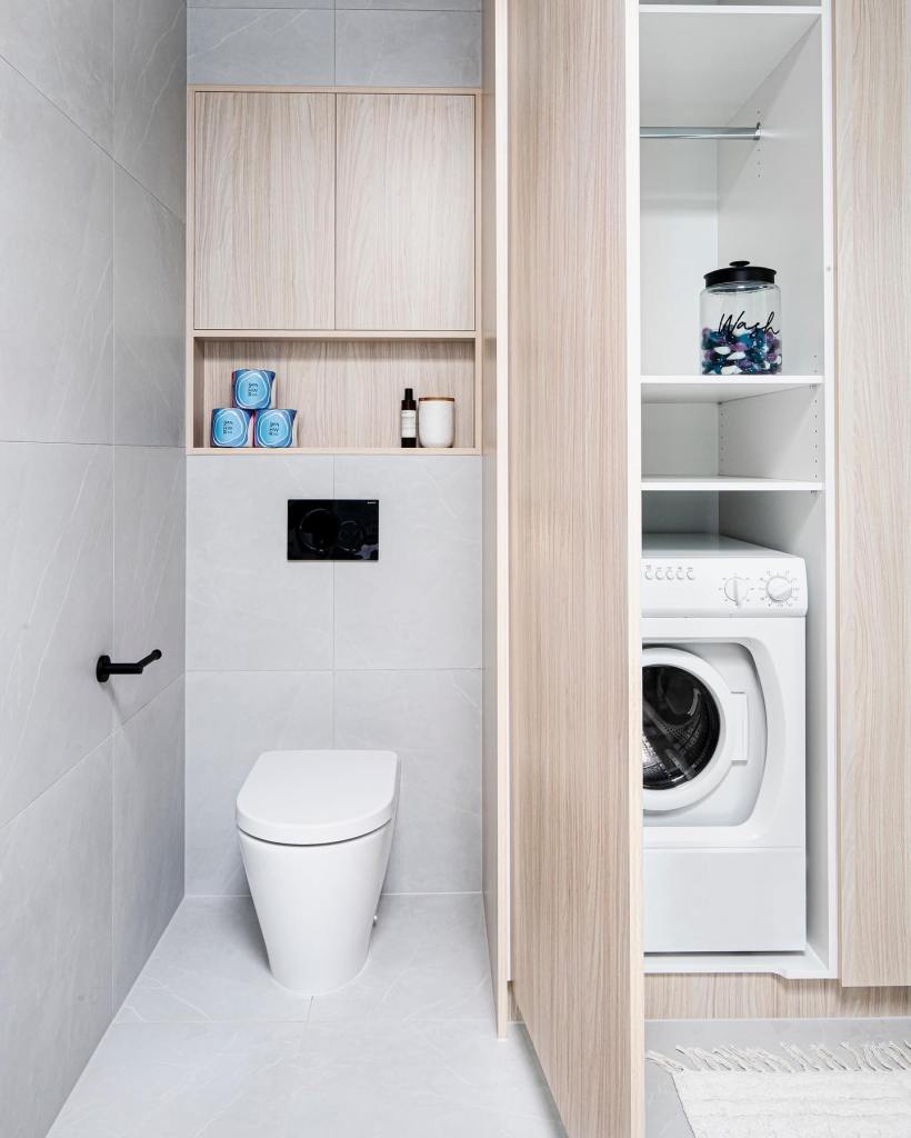 A modern and sleek bathroom featuring a white toilet against a wall tiled with large gray tiles, accompanied by a built-in...