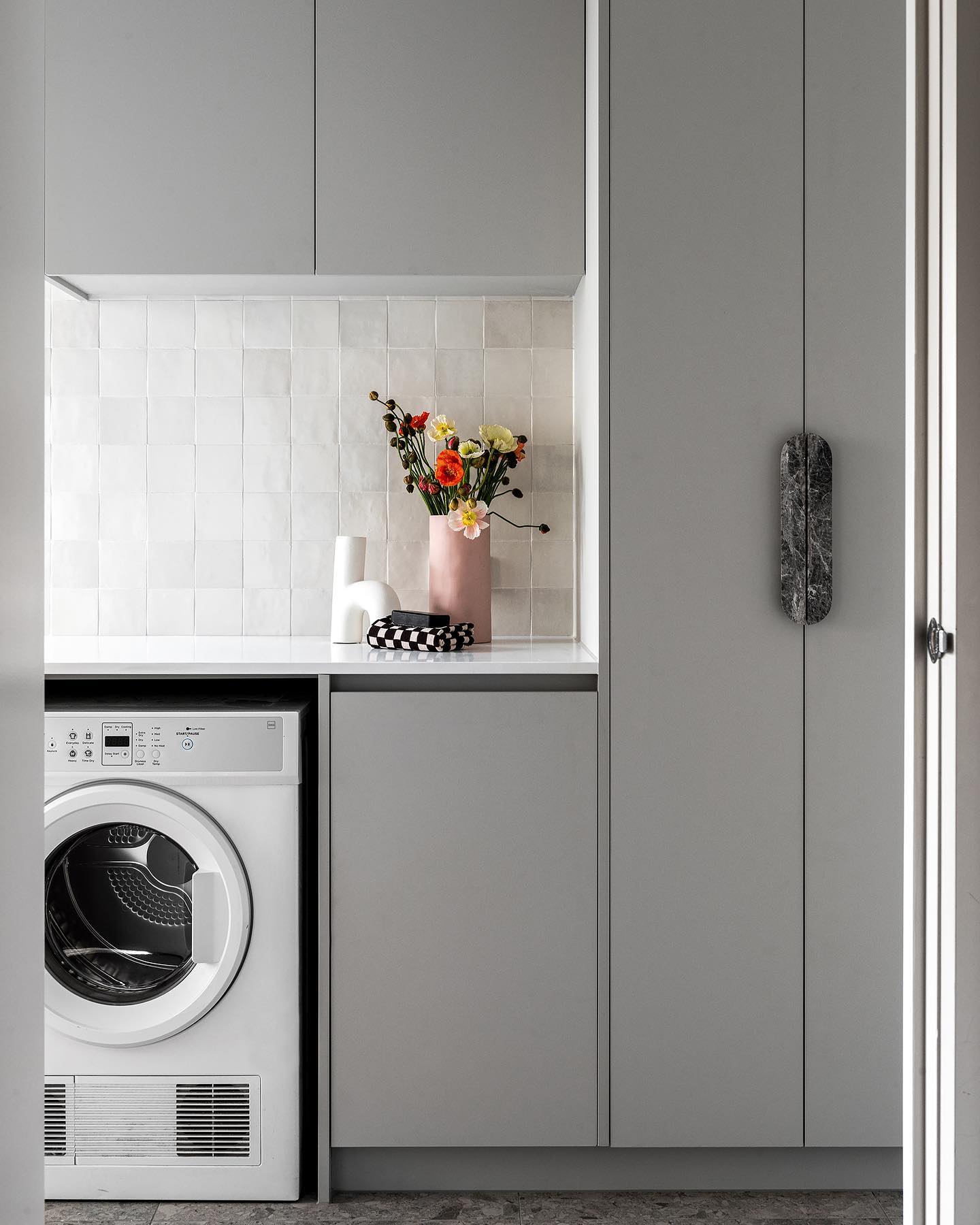 A modern laundry room, featuring a white washing machine with a digital display and instructions, compactly located within...