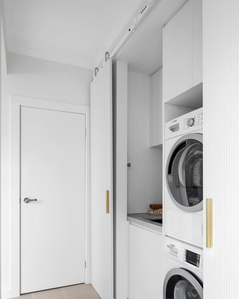 A photograph of an apartment's laundry room with a minimalist design. The washers and dryers are stacks are features of th...