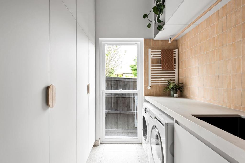 A modern laundry room features a window offering a view of an outdoor enclosure, showcasing white cabinets and a washer/dr...
